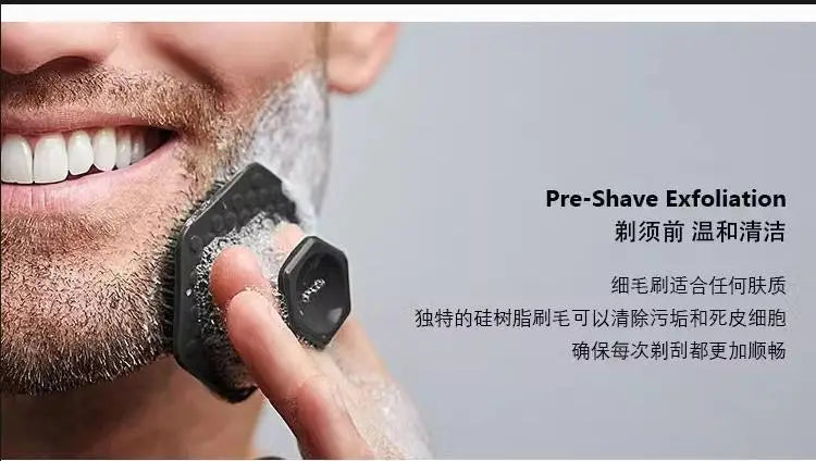 A hand is using a black silicone facial cleaning brush for pre-shave exfoliation on a man's face.
