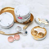 A gold tray holds a round white marble pattern contact lens storage box and a silver lens case.