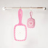 A pink detangling hair comb hanging from a metal bar.