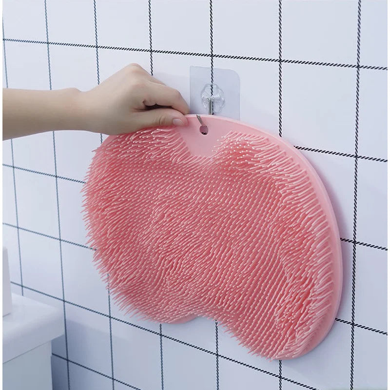 Pinker Schaum-Fuß- und Rückenpeeling mit Saugnäpfen, das an einer weißen Fliesenwand gehalten wird.