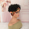 A model wears a black afro puff turban wig with an orange and green patterned fabric on a pink background.