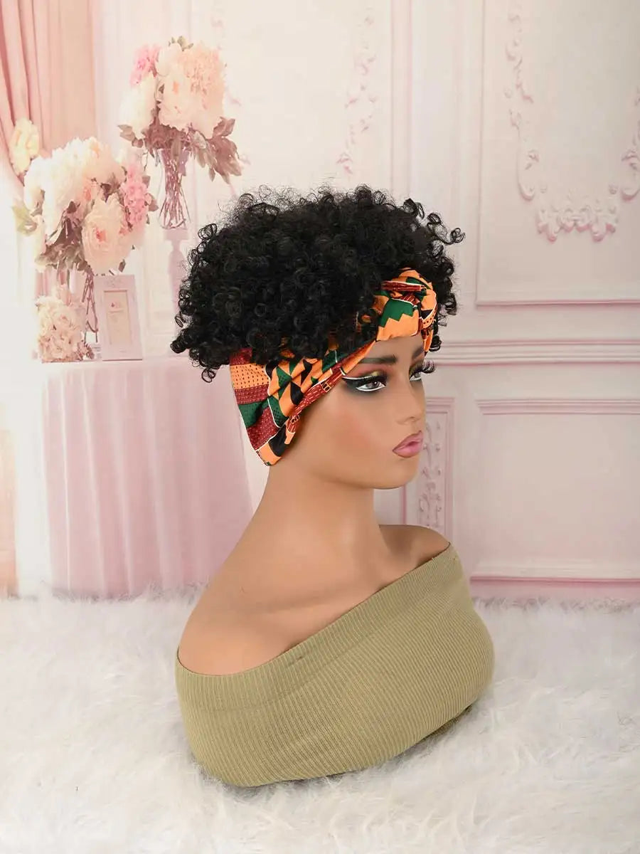A model wears a black afro puff turban wig with an orange and green patterned fabric on a pink background.