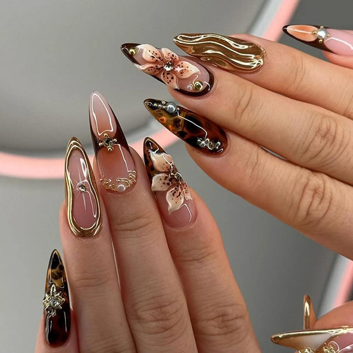 A close-up of a hand displaying various 24-piece almond press-on nails featuring floral and butterfly designs.