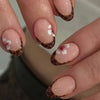 Close-up of a hand displaying press-on acrylic nails with a nude base and delicate white and pink floral accents.