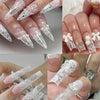 Gros plan sur des mains montrant de longues ongles acryliques décorés de décals de dentelle foil blanc et noir.