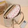A cream-colored quilted cotton makeup bag with a zipper closure and tan leather strap resting on a light surface.