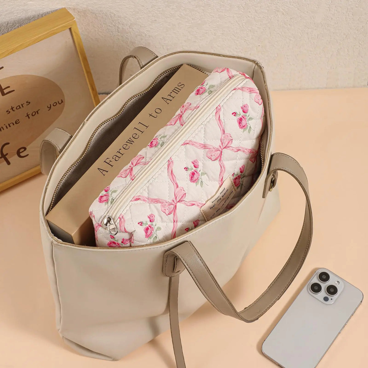A cream-colored quilted cotton makeup bag with a zipper closure and tan leather strap resting on a light surface.