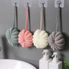 Four exfoliating bath bubble balls in pastel colors are hanging on a wall near a sink.