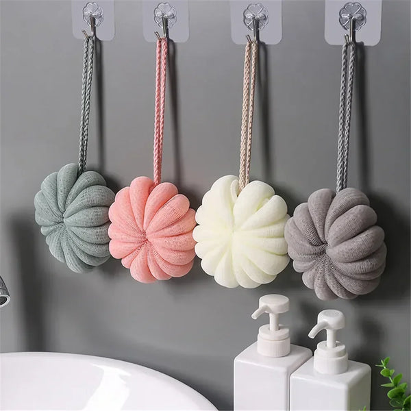 Four exfoliating bath bubble balls in pastel colors are hanging on a wall near a sink.