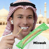Un homme portant une coiffe traditionnelle tient une brosse Miswak pour la santé bucco-dentaire.
