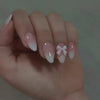 A hand displaying almond press-on nails with a sheer pink bow design on the fingernails.