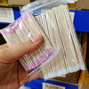 Une main tient un sac plastique transparent rempli de nombreux cotons-tiges à double pointe pour enlever le vernis à ongles.
