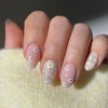 A hand displays a set of press-on acrylic nails with a sheer pink base and delicate white flower accents.