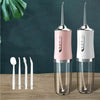 A white and pink precision electric water floss and oral irrigator device standing in a clear holder on a wooden surface.