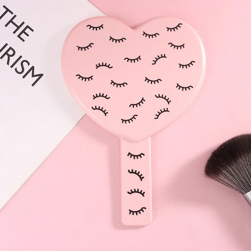 Miroir à main en forme de cœur rose avec des cils noirs.