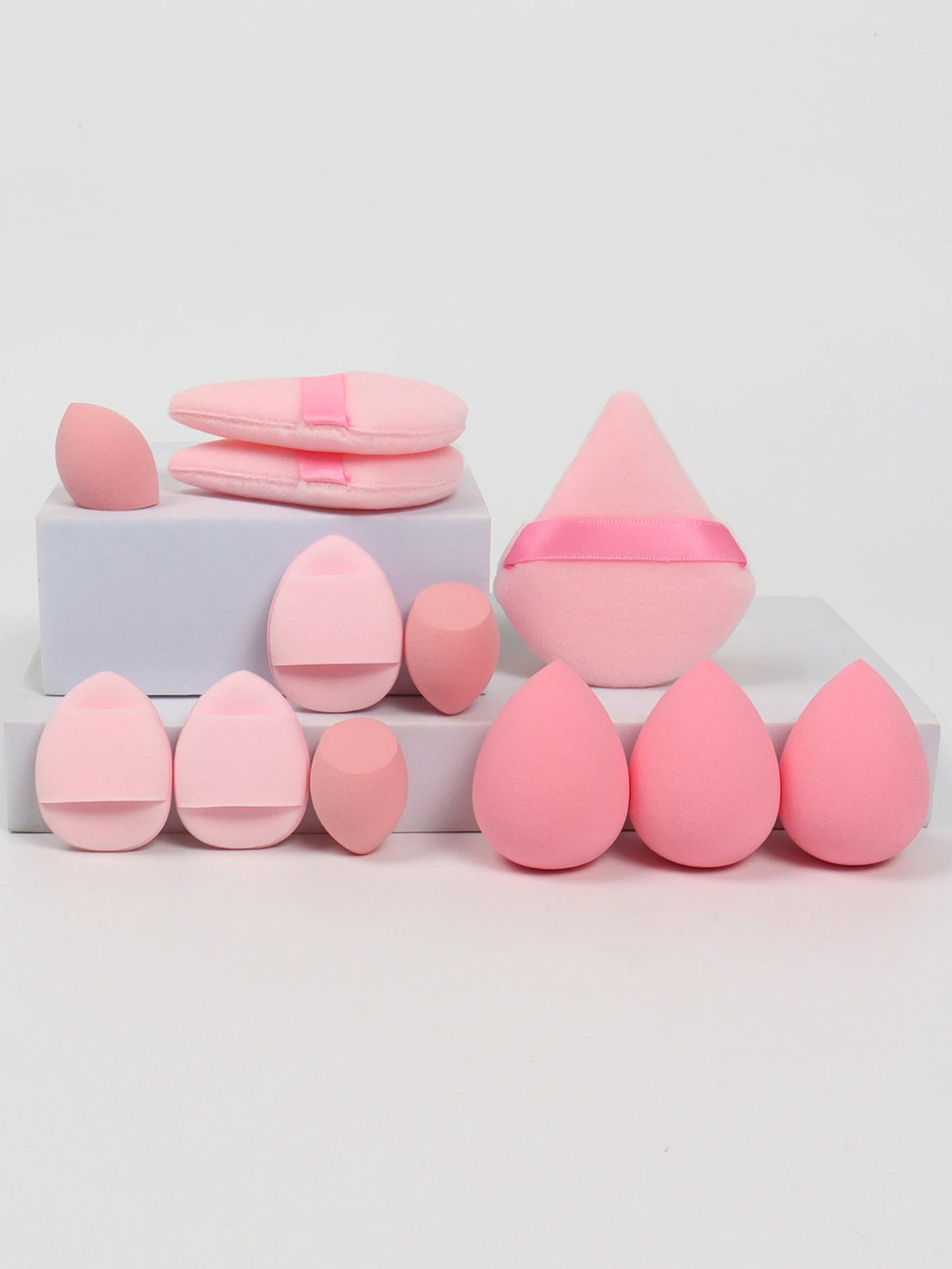 A set of twelve pink makeup sponges in various shapes and sizes arranged on a white surface.