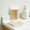 A clear plastic container holds numerous wooden cotton swabs next to a white pump bottle.