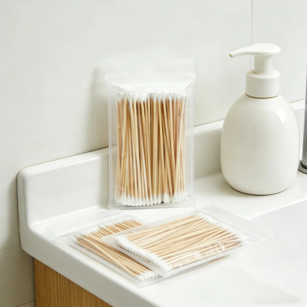 A clear plastic container holds numerous wooden cotton swabs next to a white pump bottle.