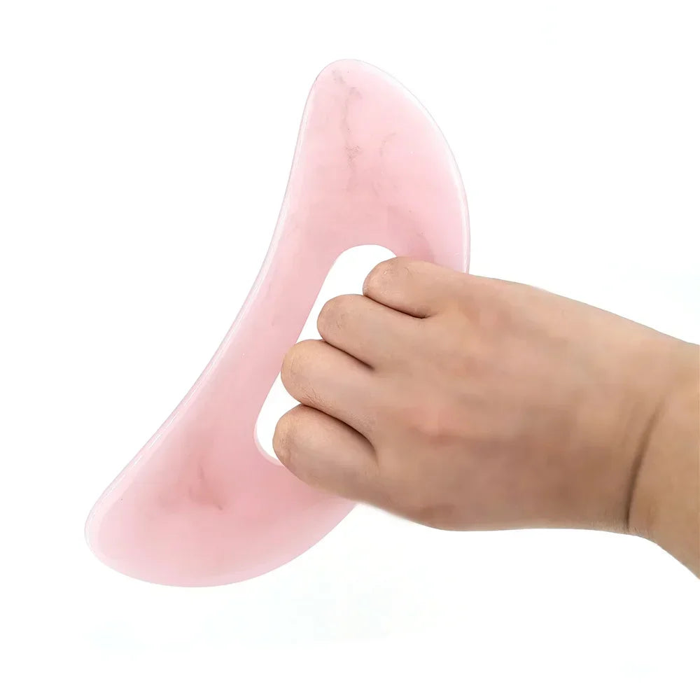 Une main tient un board de massage guasha en pierre naturelle rose et lisse.