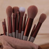 A collection of 22 professional makeup brushes in various shades of brown and gray are displayed on a neutral fabric.