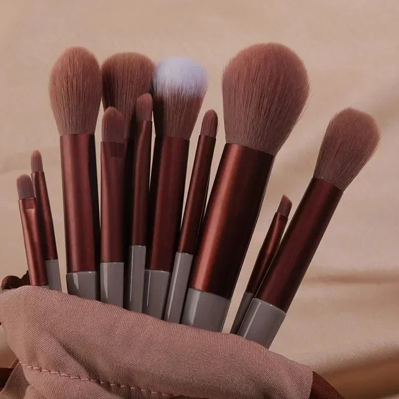 A collection of 22 professional makeup brushes in various shades of brown and gray are displayed on a neutral fabric.