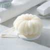 A white exfoliating bath bubble ball with a soft mesh sponge is shown on a white surface next to a white towel and a white si