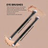 A set of two dual-ended eyeshadow brushes shown with loose makeup powder on a beige background.