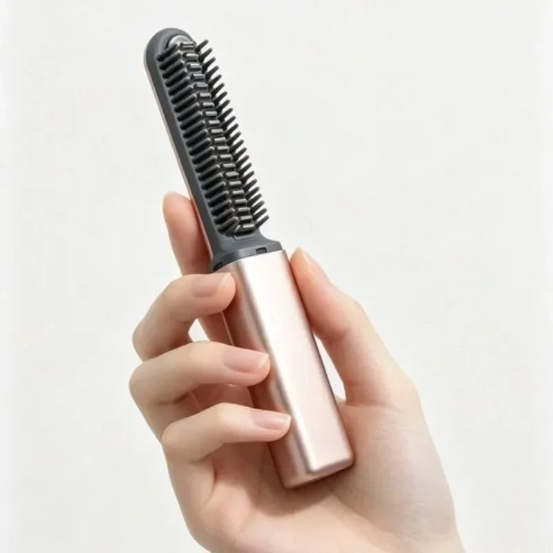 A hand holds a portable wireless hair comb and curling iron with a pink body and black bristles.