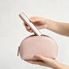 A person holds a pink portable wireless hair comb and curling iron against a light background.