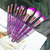 A set of ten professional makeup brushes with purple and pink bristles displayed on a dark green background.