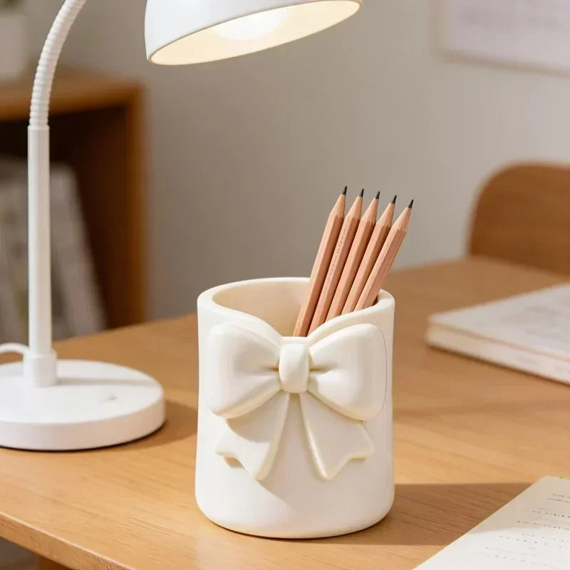 Un organisateur de rangement décoratif blanc en forme de nœud tient plusieurs crayons en bois sur un bureau en bois clair.