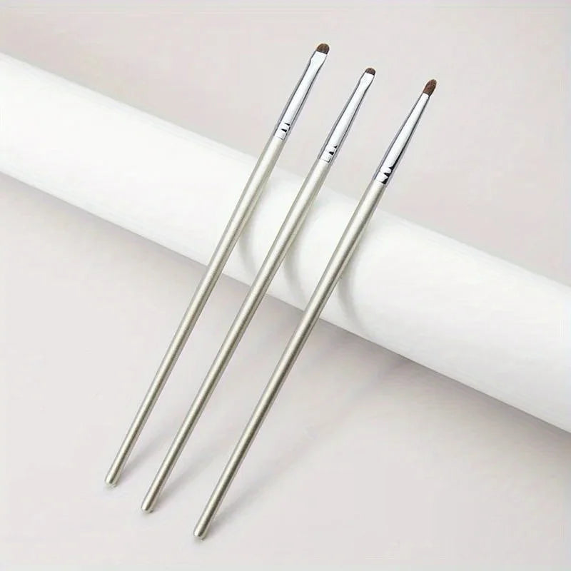 Three silver precision eyeshadow brushes lying on a white cylindrical surface.