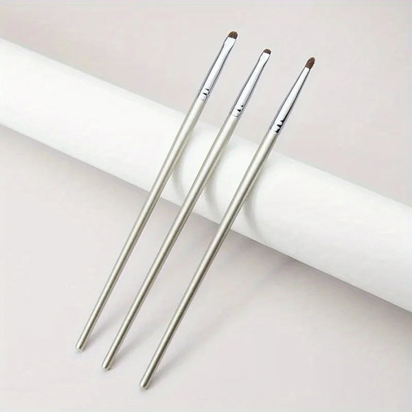 Three silver precision eyeshadow brushes lying on a white cylindrical surface.